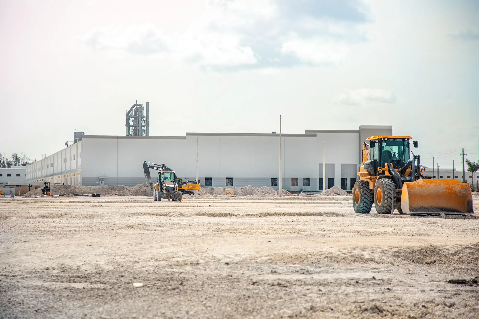 Cleared ground and earthmoving equipment beside an existing industrial building
